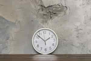 Free photo round clock face leaning against damaged concrete wall on wooden desk