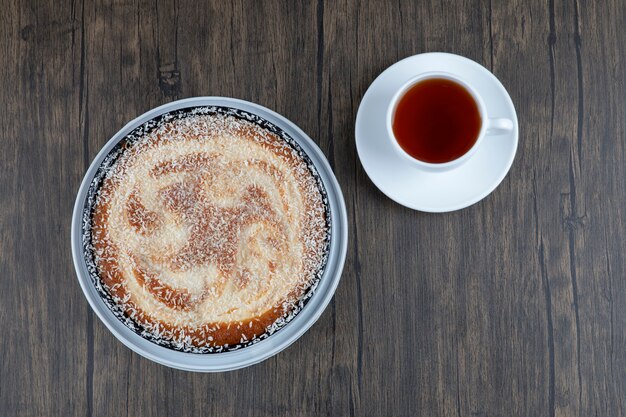 Round delicious cake with a cup of tea placed on a wooden table. 