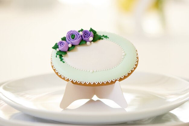 Круглые имбирные пряники, покрытые белой глазурью и украшенные фиолетовыми цветами, стоят и узором на тарелках у фужеров на праздничном свадебном столе. Фото было сделано