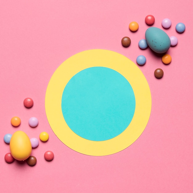 Foto gratuita cornice di carta rotonda decorata con caramelle gemma e uova di pasqua su sfondo rosa