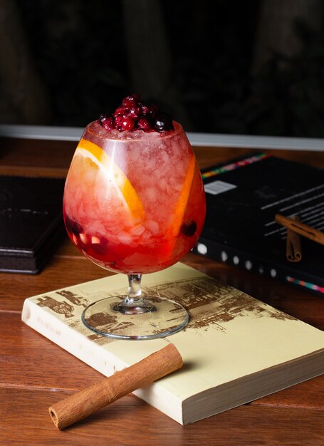 A round-shaped glass with berry cocktail with orange slices