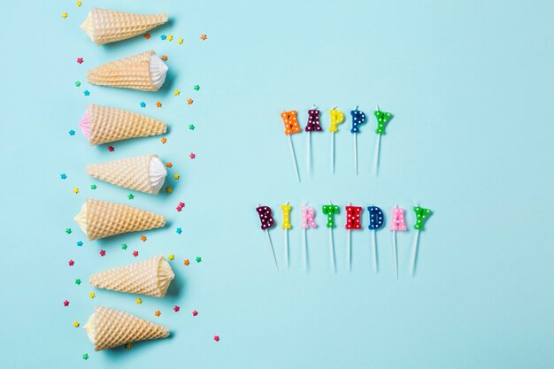 Row of aalaw in the waffle cone with sprinkles near the happy birthday candles on blue background