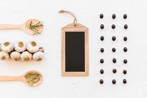 Row of black olives with empty black slate and bunch of garlic bulbs