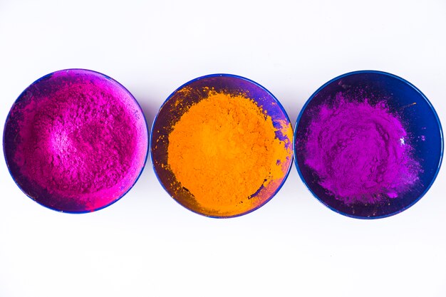 Row of blue bowls with purple; orange and pink holi color powder on white backdrop