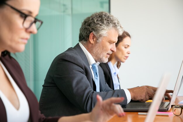 Row of business people using computers in office. Employees of different ages typing on laptop keyboards.