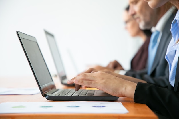 Row of business people working at computers. Hands of employees typing on laptop keyboards.