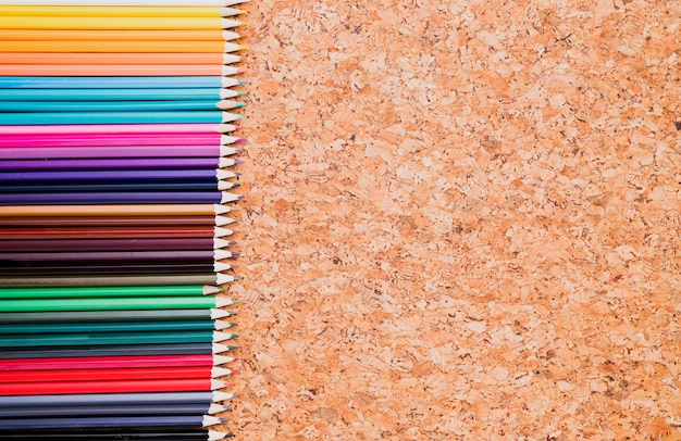 Free photo row of color pencils on cork background top view