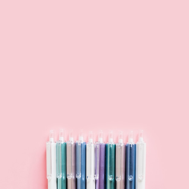 Row of colorful pens on pink background