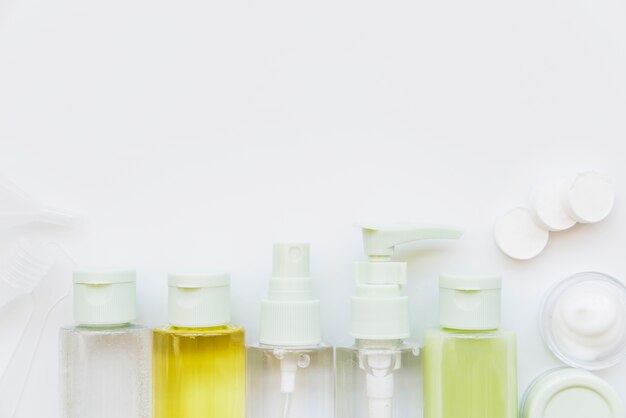 Row of cosmetic spray bottle with closed lid and moisturizer against white backdrop