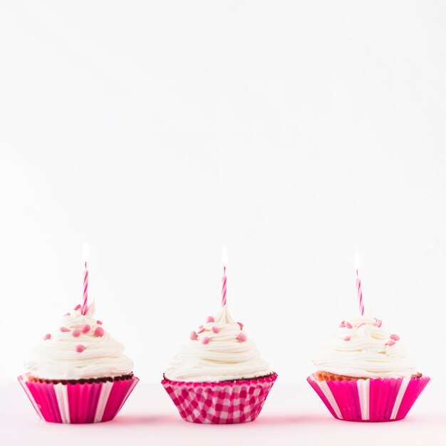 Row of fresh cupcakes with burning candles against white background