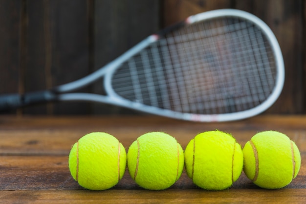 Foto gratuita fila delle palline da tennis verdi davanti alla racchetta vaga sulla tavola di legno