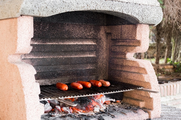 Foto gratuita fila di salsicce alla griglia su barbecue portatile all'aperto