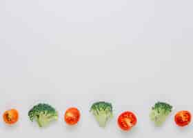 Free photo row of halved cherry tomatoes and green broccoli on the bottom on white backdrop