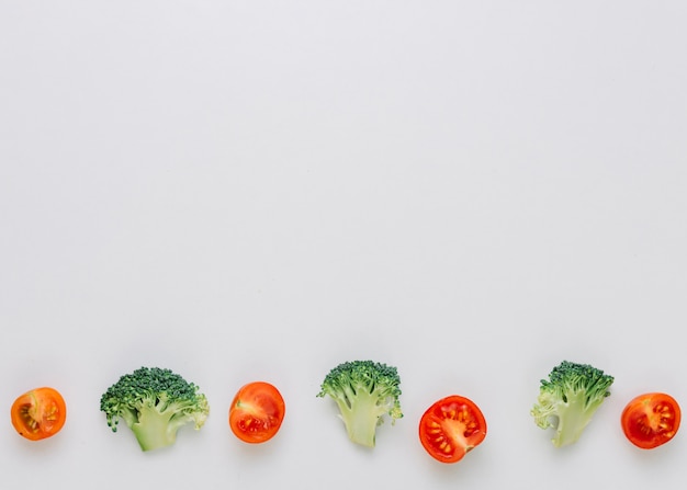 Row of halved cherry tomatoes and green broccoli on the bottom on white backdrop