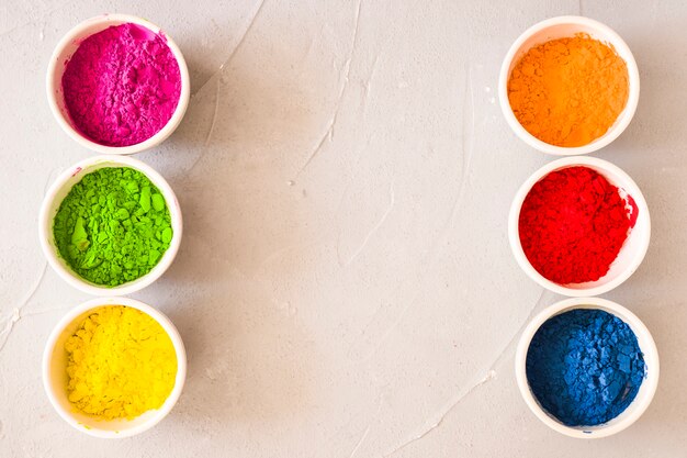 Row of holi color powder white bowls on textured backdrop