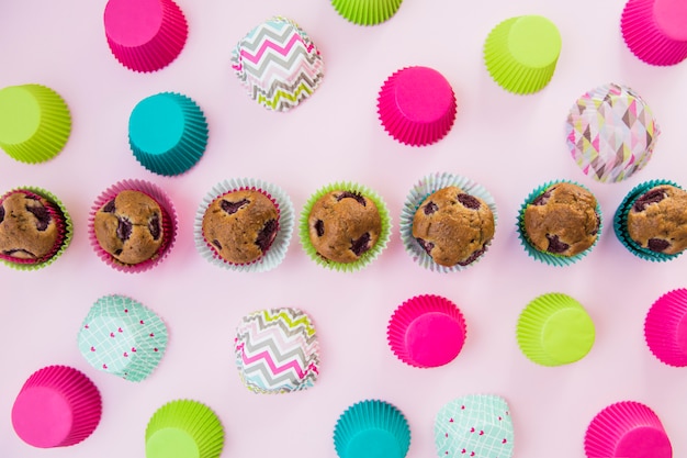 Fila di cupcakes fatti in casa circondato con carta colorata titolare su sfondo rosa