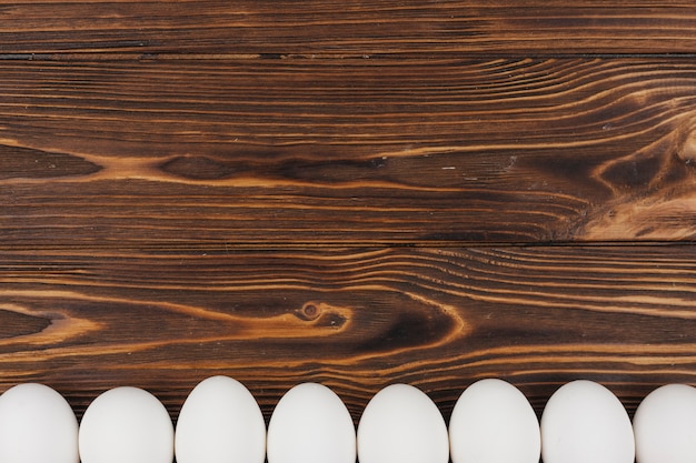Бесплатное фото Ряд белых куриных яиц на коричневый деревянный стол