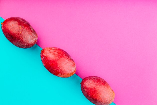 Row of red mangoes on dual pink and blue background