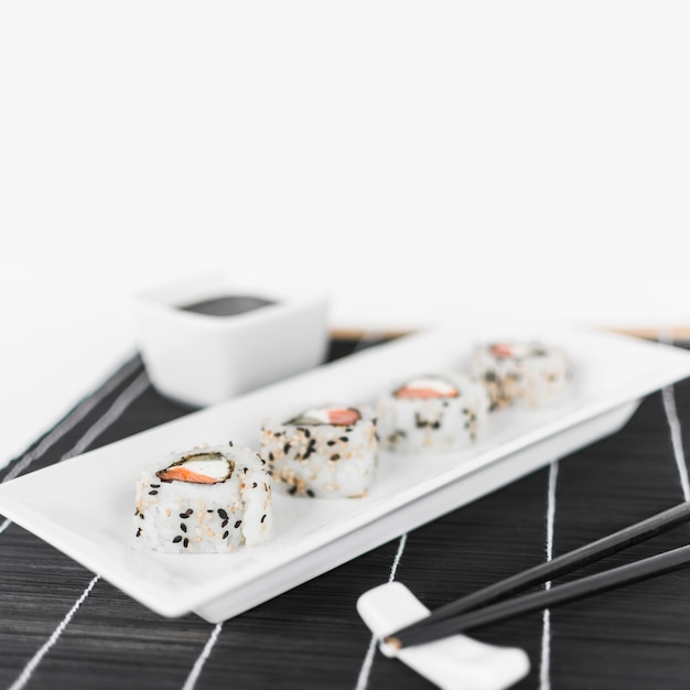 Row of sushi on white tray with chopsticks