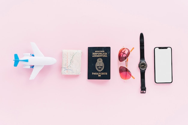 Row of toy airplane; folded map; passport; sunglasses; wrist watch and smartphone on pink background