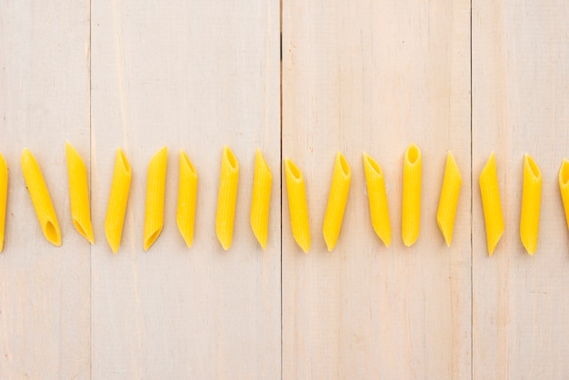 Row of uncooked penne pasta over wooden plank