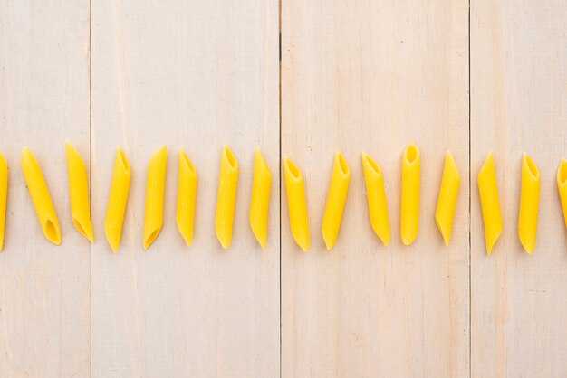 Row of uncooked penne pasta over wooden plank