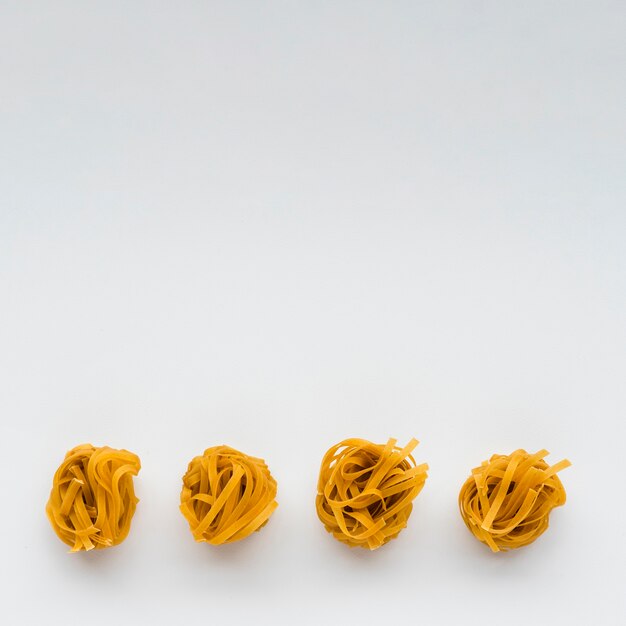 Row of uncooked tagliatelle pasta at the bottom of white background