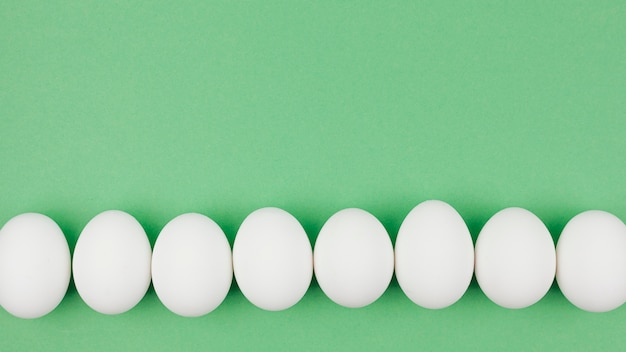 Row of white chicken eggs on green table