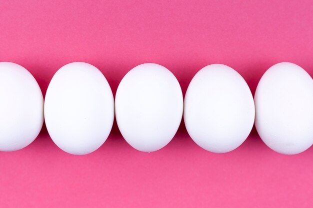 Row of white chicken eggs on pink table