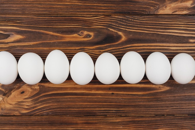 Row of white chicken eggs on wooden table