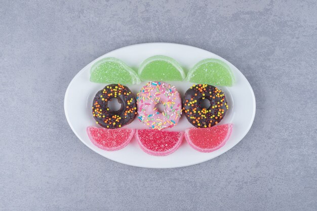 Rows of donuts and marmelades on a platter on marble surface