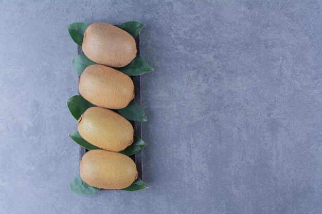 Rows of kiwi fruits with leaves on the board on marble table.