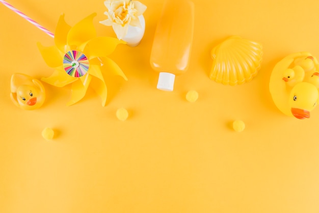 Бесплатное фото Резиновая утка; вертушка; бутылка солнцезащитного крема; морской гребешок с маленьким помпоном на желтом фоне