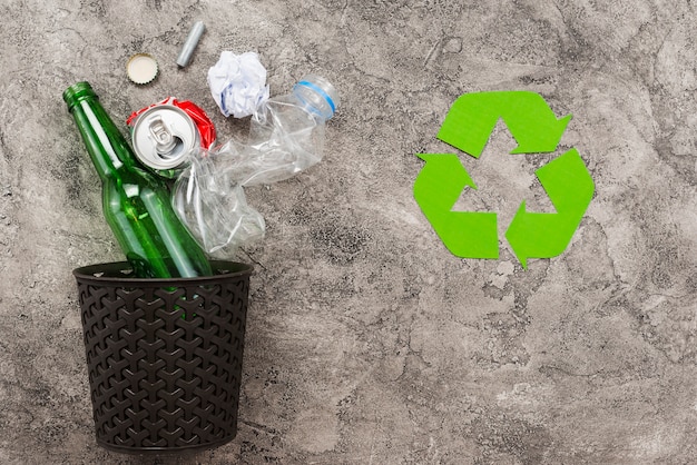 Rubbish bin with trash beside recycling logo