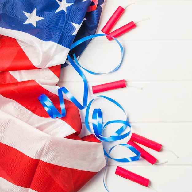 Ruffled american flag; blue ribbon and dynamite firecrackers on wooden table