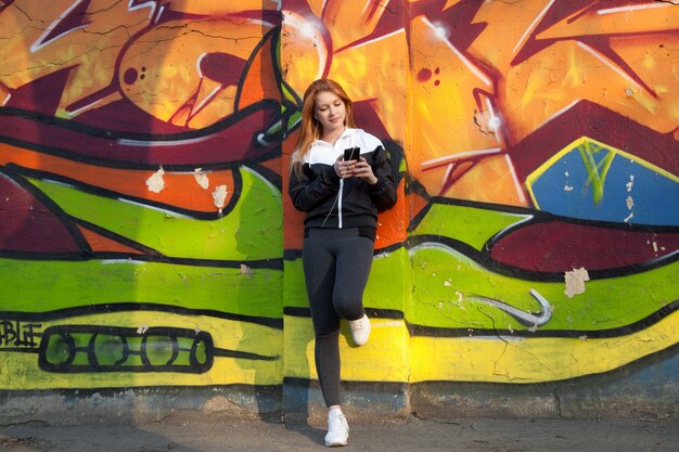 Runner girl resting with mobile phone against bright graffiti wall