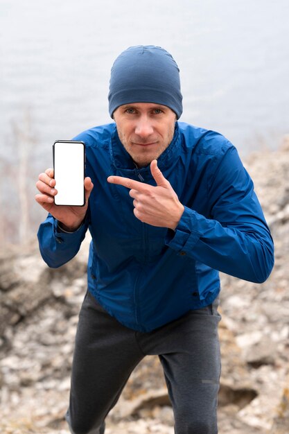 Runner man showing blank phone in nature