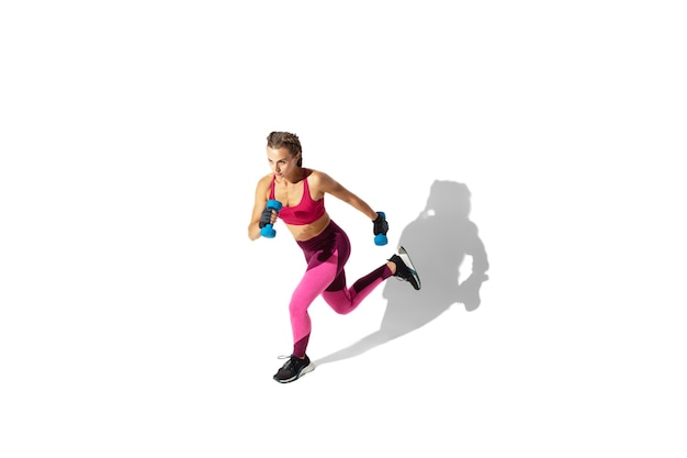 Running. Beautiful young female athlete practicing on white  wall, portrait with shadows. Sportive fit model in motion and action. Body building, healthy lifestyle, style concept.