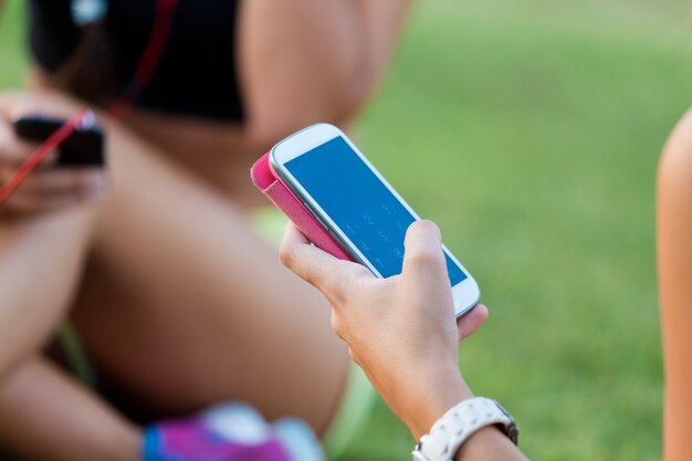 Running girls having fun in the park with mobile phone.