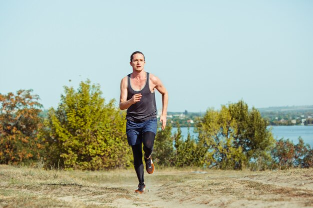 Бег спорт. Бегущий человек спринте открытый в живописной природе. Приспособьте мускулистую мужскую спортивную тренировочную тропу, бегущую для пробега марафона Спортивный здоровый атлетик работает в сжатой одежде в спринте