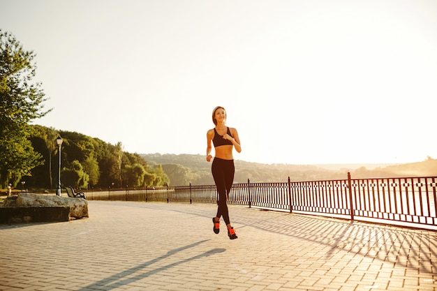 Running woman. Runner jogging in sunny bright light. Female fitness model training outside in park