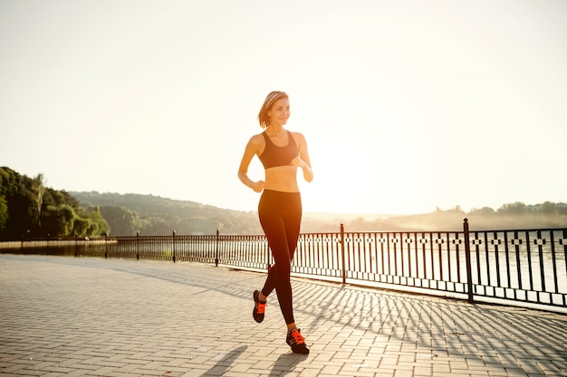 走っている女性。日当たりの良い明るい光の中でジョギングランナー。公園の外の女性フィットネスモデルトレーニング