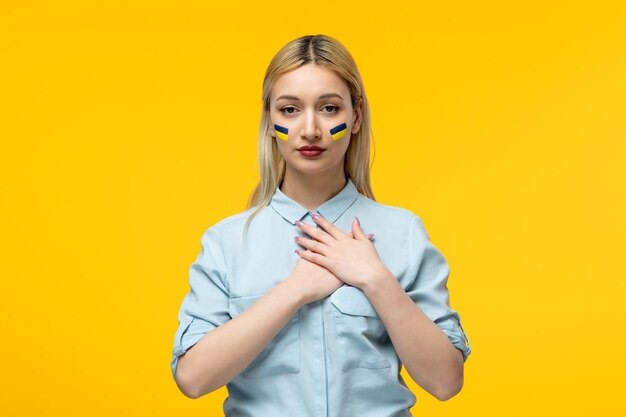 Russian ukrainian conflict cute girl yellow background with ukrainian flag on cheeks holding chest