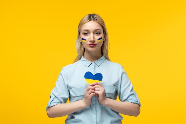 마음을 잡고 뺨에 우크라이나 국기와 러시아 우크라이나 충돌 귀여운 소녀 노란색 배경