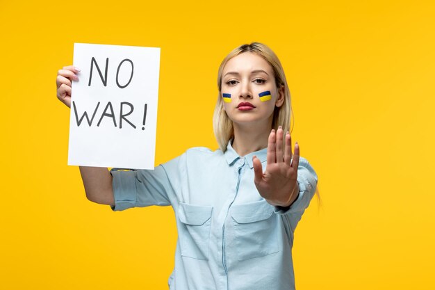 러시아 우크라이나 충돌 귀여운 소녀 노란색 배경에는 전쟁이 없는 뺨에 우크라이나 국기가 있습니다.