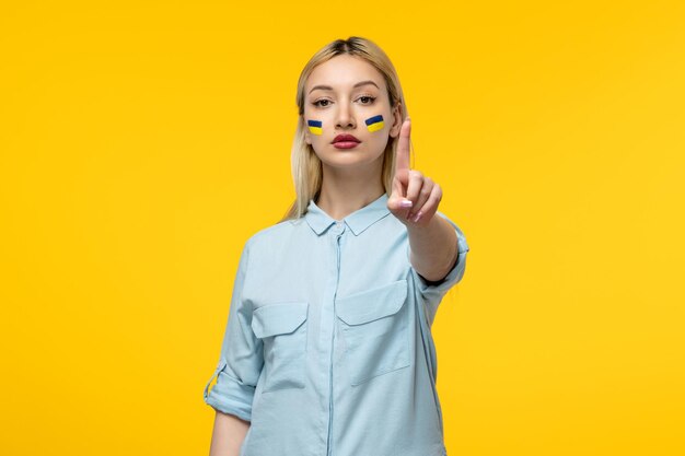 Russian ukrainian conflict cute girl yellow background with ukrainian flag cheeks pointing finger