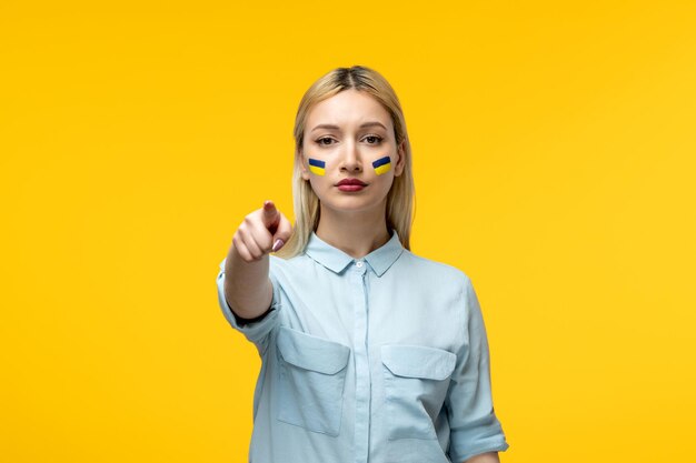 Russian ukrainian conflict cute girl yellow background with ukrainian flag on cheeks pointing finger