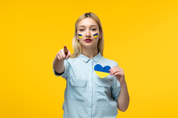 Russian ukrainian conflict cute girl yellow background with ukrainian flag on cheeks pointing finger