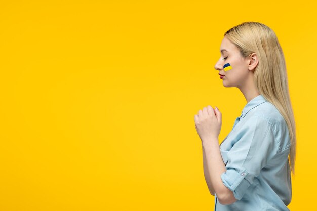 Russian ukrainian conflict cute girl yellow background with ukrainian flag on cheeks praying