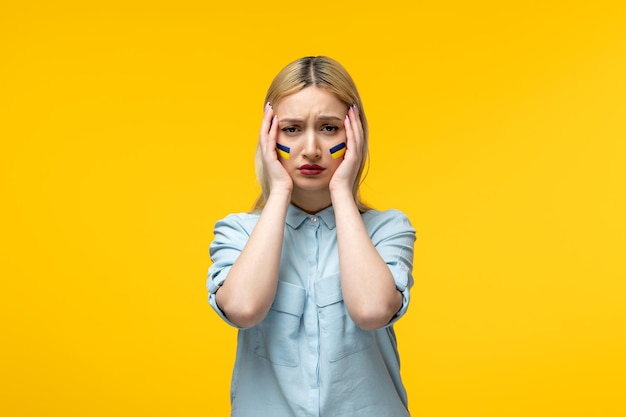 Russian ukrainian conflict cute girl yellow background with ukrainian flag on cheeks scared